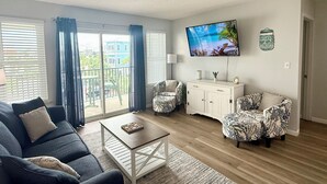 Un salon comprenant un canapé, deux fauteuils à motifs, une table basse, un téléviseur et un meuble.