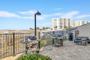 Une terrasse avec des barbecues, une poubelle et une table.