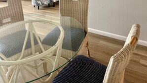 Un coin repas avec des chaises en osier et une table en verre, un meuble blanc et un téléviseur fixé au mur.