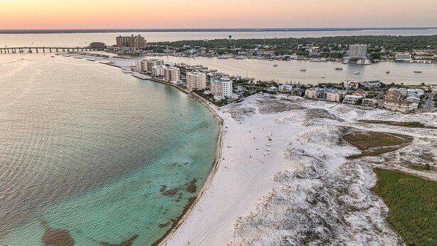 Vue aérienne d’une ville côtière avec une plage remarquable, un port de plaisance et un pont la reliant à la terre ferme.