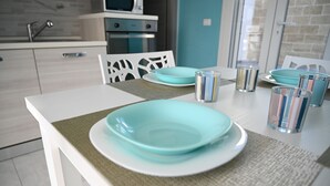 Eine moderne Küche mit weißen Schränken, einem eingebauten Backofen und einem Essbereich mit einem weißen Tisch, gedeckt mit türkisfarbenen Tellern und Gläsern.