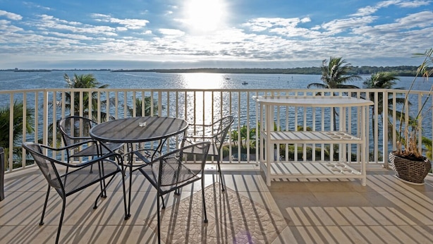 A balcony with a view of the sea, featuring a round table and chairs, a white bench, and a potted plant. - Spectacular Sunset Views! Watch Dolphin from Your Balcony ! (St. Petersburg)