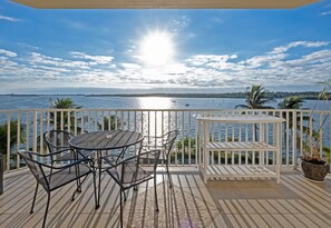 A balcony with a view of the sea, featuring a round table and chairs, a white bench, and a potted plant. - Spectacular Sunset Views! Watch Dolphin from Your Balcony ! (St. Petersburg)