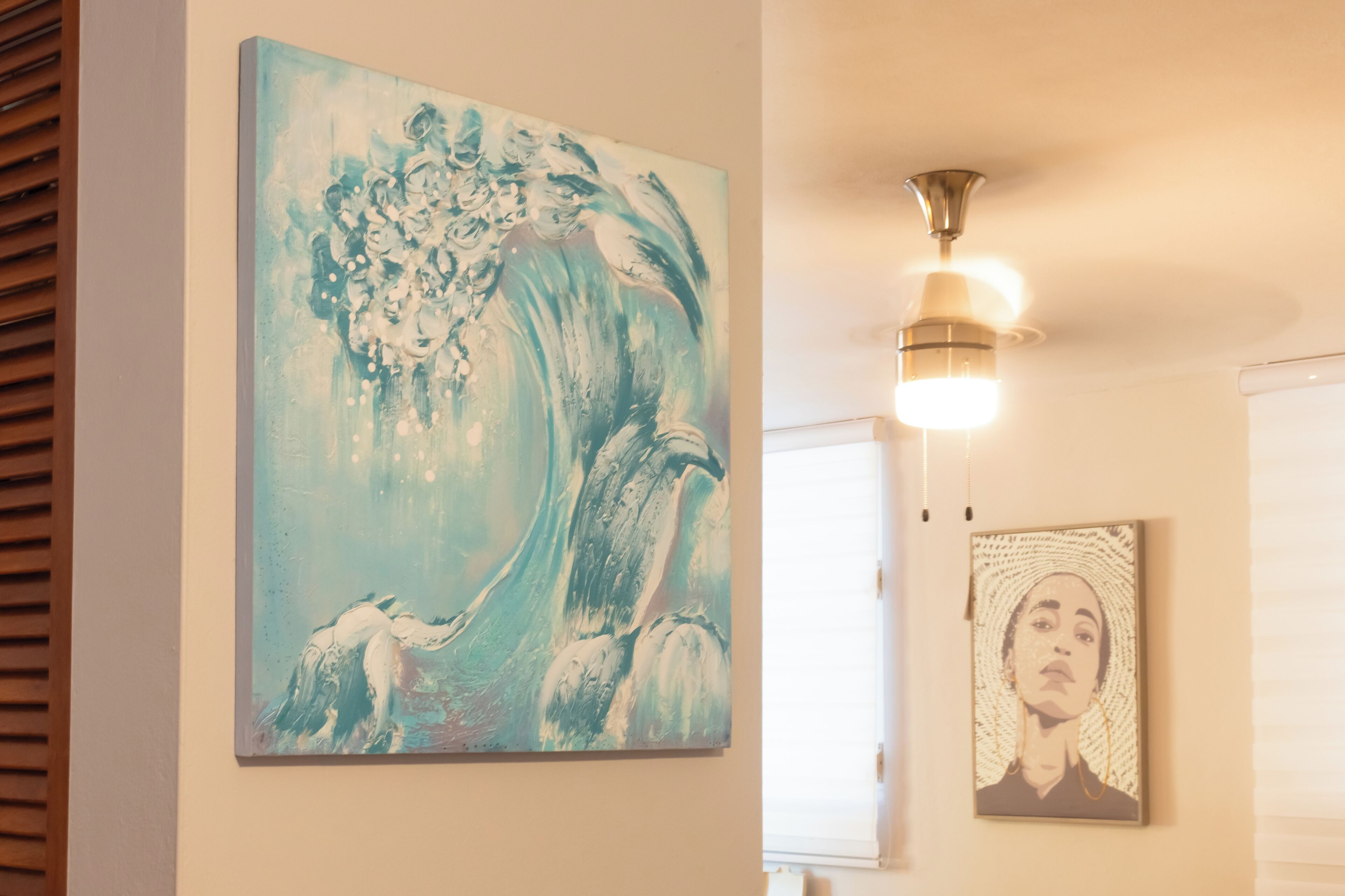 Een kamer met een groot abstract schilderij aan de muur, een plafondlamp en een kleiner ingelijst kunstwerk daaronder.