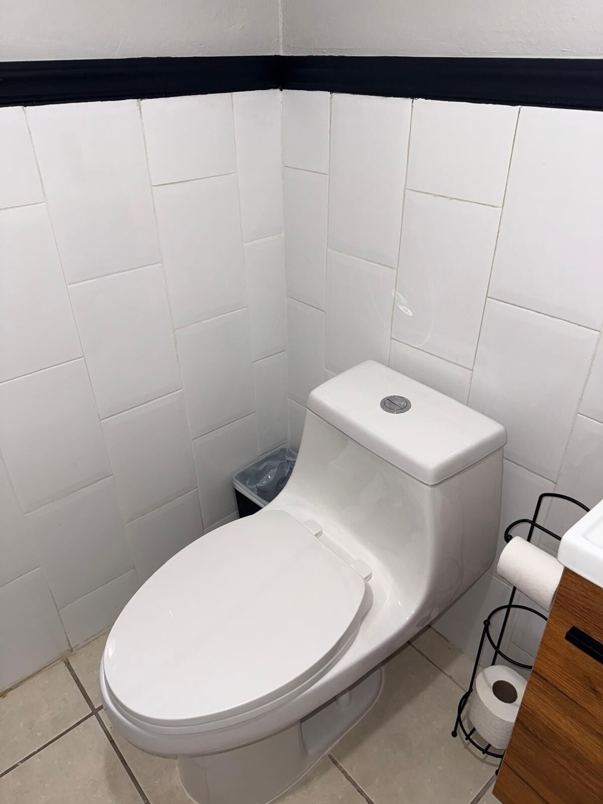 A standard white toilet with a tank, a small trash bin, and a toilet paper holder.