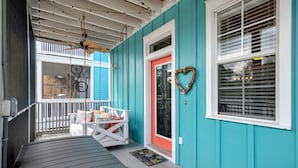 Een overdekte veranda met een bank, een witte balustrade en een turquoise muur.
