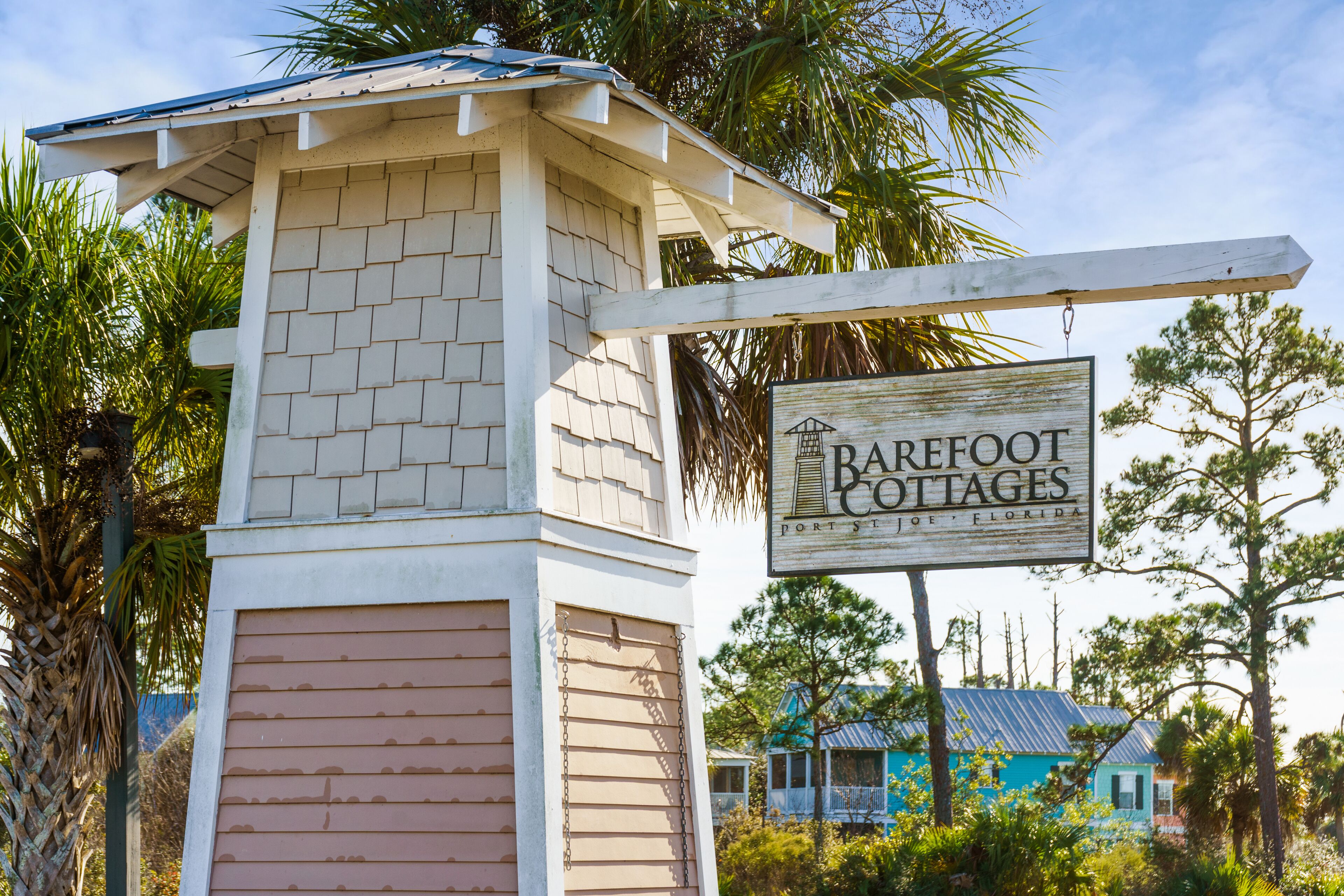 A sign for Barefoot Cottages in Port St. Joe, Florida, with a rustic building and palm trees in the background.