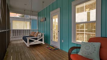 Relax on the porch with a swing seat and a wicker chair, surrounded by two windows with white shutters.