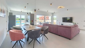 Een moderne woonkamer met een eetgedeelte, een roze bank en een aan de muur bevestigde televisie.