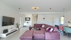Een moderne woonkamer met een grote hoekbank, een flatscreen televisie en een eethoek met een tafel en stoelen.