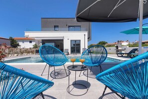 A modern outdoor pool area with two blue chairs, a table, and two drinks.
