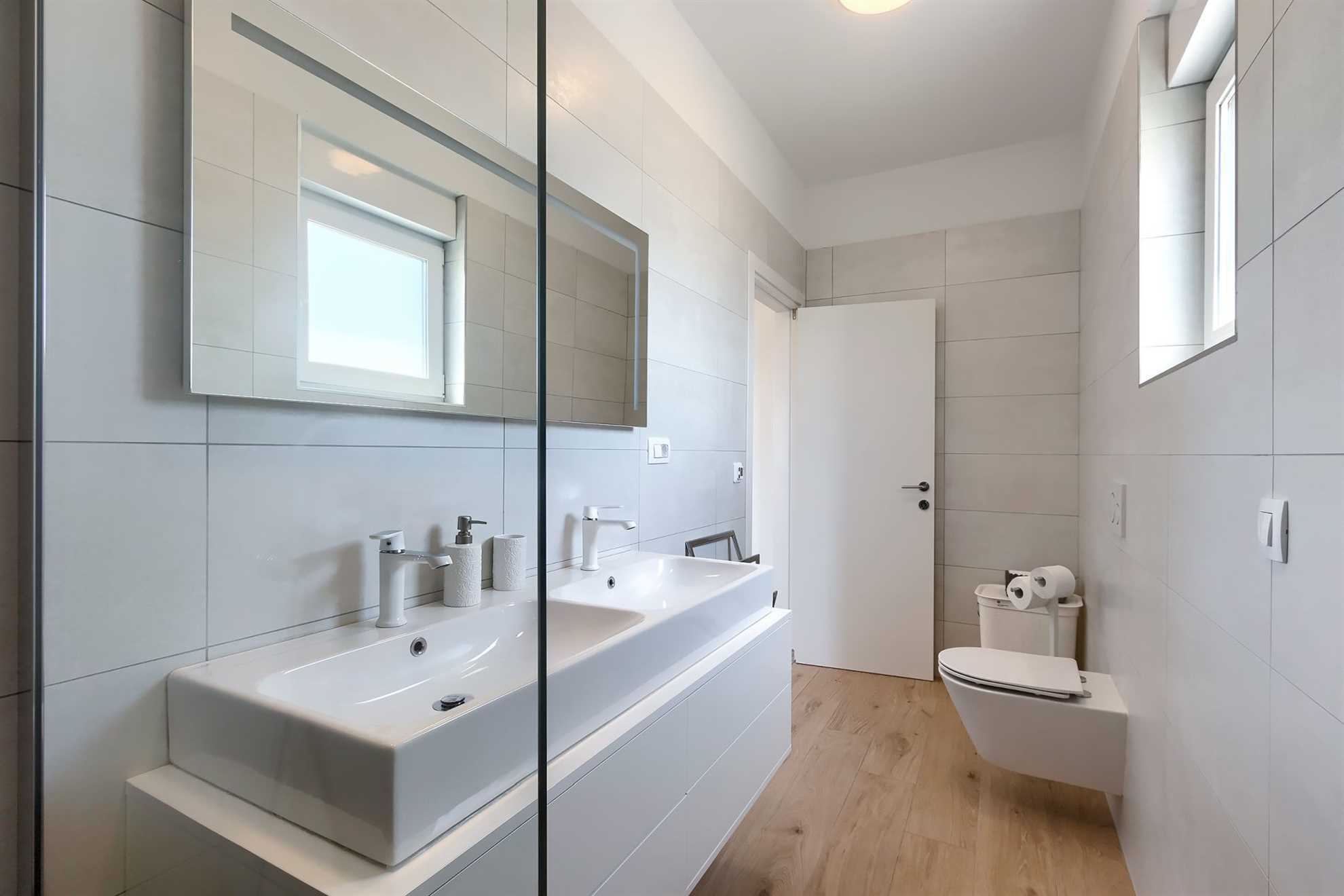 A modern bathroom with two sinks, a toilet, and a shower.