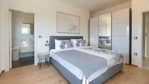 Een moderne slaapkamer met een groot bed, een nachtkastje, een stoel, een kledingkast en een spiegel.