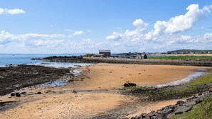 A coastal beach with a sandy shore, rocky outcrops, and a clear blue sky.