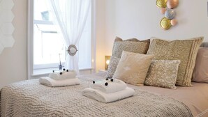 Un lit bien fait, recouvert d’une couverture beige à texture intéressante, avec deux serviettes pliées et plusieurs coussins à motifs.