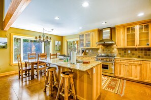 A spacious kitchen with wooden cabinets, a large island with stools, a stainless steel stove, and a view through the windows.