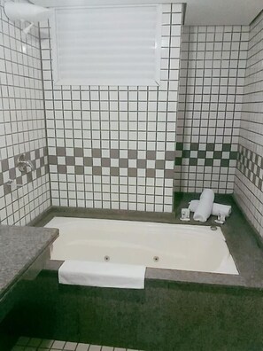 Een badkamer met een bad, douche en toilet. Er liggen handdoeken en een fles op het aanrecht.