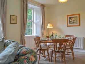 Un coin repas avec une table dressée pour quatre personnes, entouré de chaises en bois, d’une lampe et d’une fenêtre avec des rideaux.