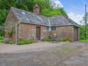 A stone cottage with a tiled roof, a small garden, and a table with chairs outside.