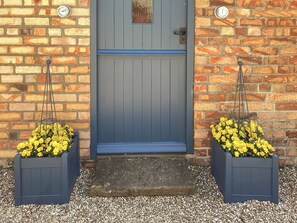 Una puerta azul con una pequeña ventana encima, flanqueada por dos macetas con flores amarillas.