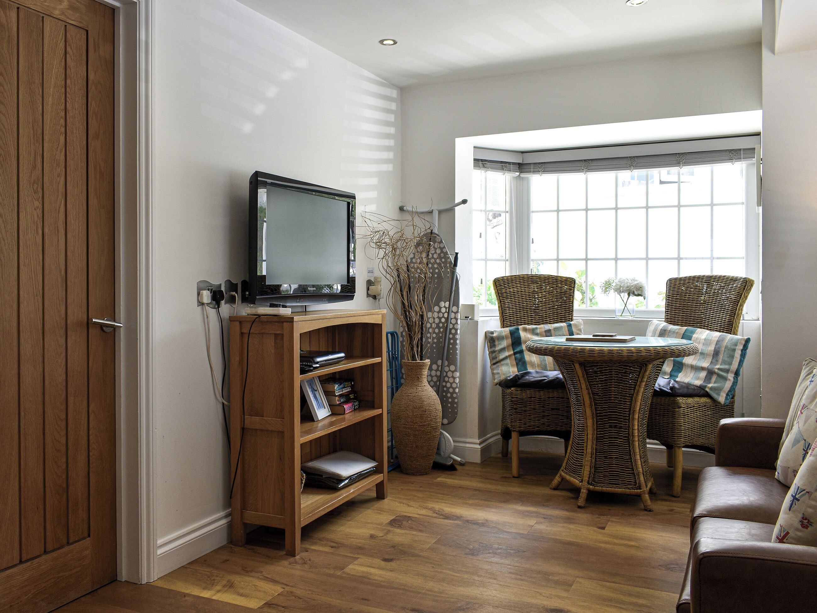 A living room with a television on a wooden stand, wicker furniture, and a large window with blinds.