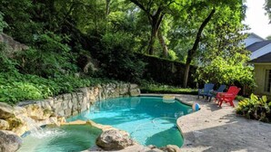 Una piscina con borde de piedra, rodeada de abundante vegetación y árboles.