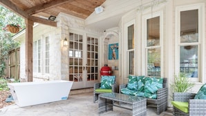 Un patio techado con mobiliario de mimbre, una bañera blanca y suelo de piedra.