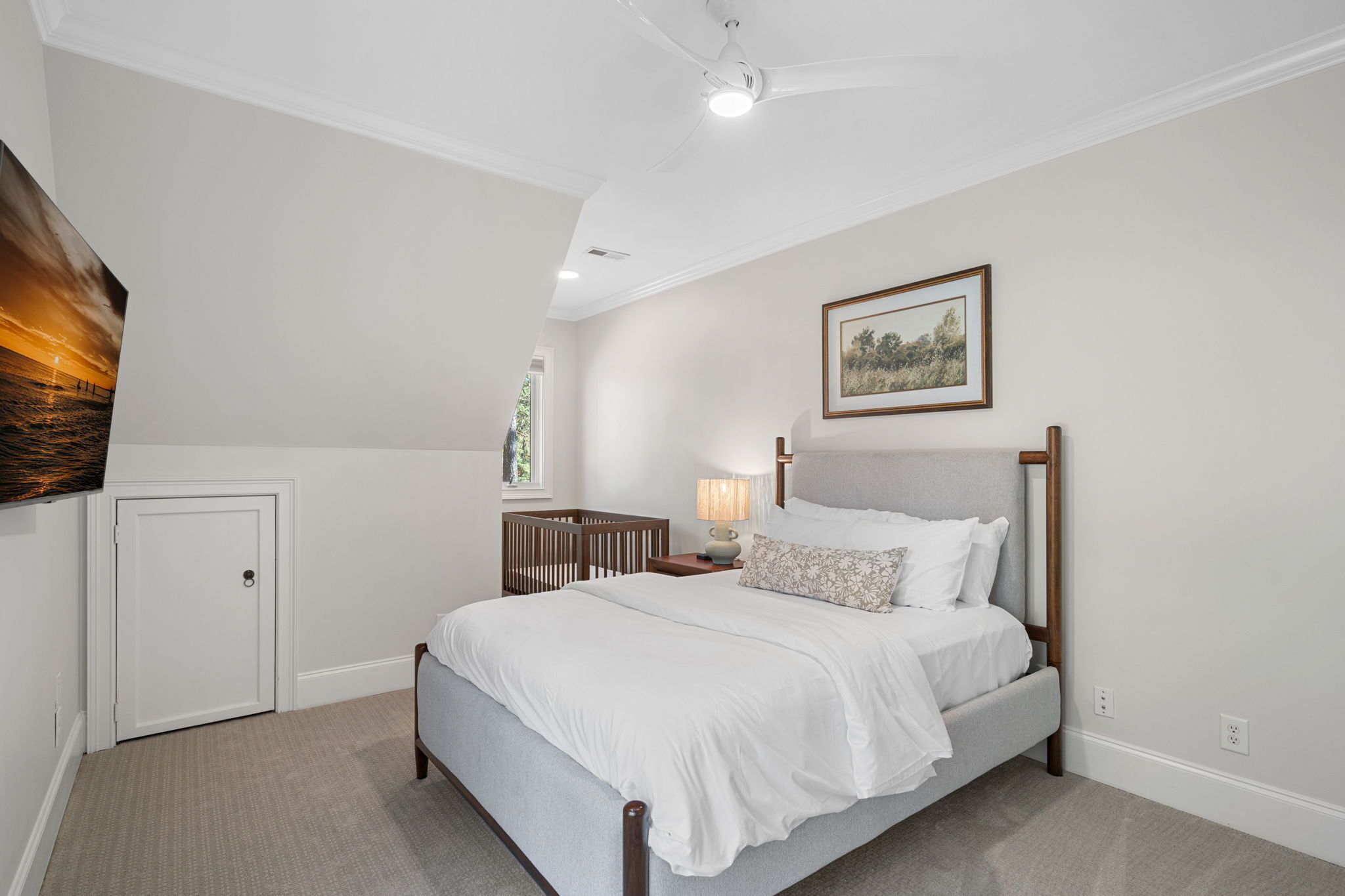 Un dormitorio con cama, mesita de noche, lámpara, cuna y una puerta.