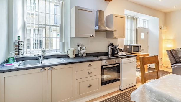Eine moderne Küche mit Backofen, Mikrowelle und Kaffeemaschine. Es gibt ein Fenster mit Jalousien, ein Spülbecken und einen Holzbalken an der Decke.