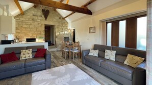 A spacious living room with a stone fireplace, wooden beams, a dining area, and a large window.