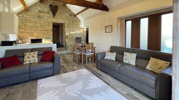 A spacious living room with a stone fireplace, wooden beams, a dining area, and a large window.