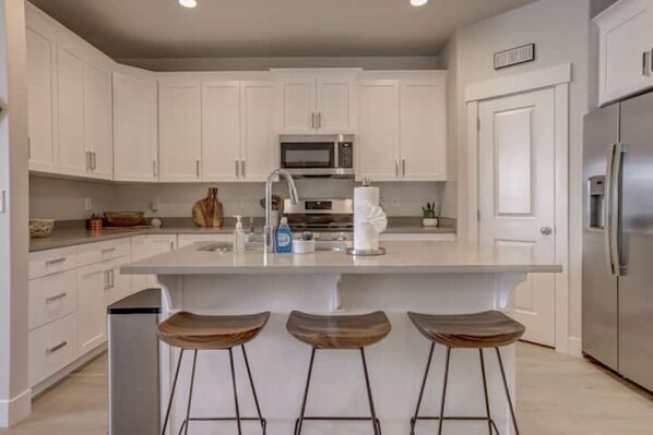 A modern kitchen with white cabinets, a central island with stools, stainless steel appliances, and a door with a sign. - Gateway to Zion-Beautiful BRAND NEW 3 bed/2.5 bath (Washington)