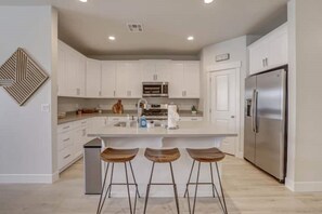 A modern kitchen with white cabinets, a stainless steel refrigerator, and a central island with stools. - Gateway to Zion-Beautiful BRAND NEW 3 bed/2.5 bath (Washington)