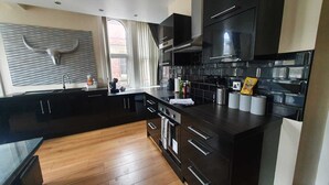 A modern kitchen with dark cabinetry, a wooden floor, and a window with curtains. - Contractor Mid week bookers (Liverpool)