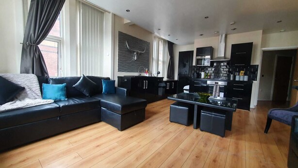 A modern living room with a black sofa, a dining area with a black table, and a kitchen with black cabinets and stainless steel appliances. - Contractor Mid week bookers (Liverpool)