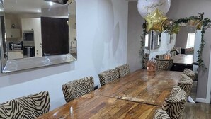 A dining area with a long wooden table, zebra-patterned chairs, a large mirror, and a festive balloon arrangement. - Contractor Mid week bookers (Liverpool)