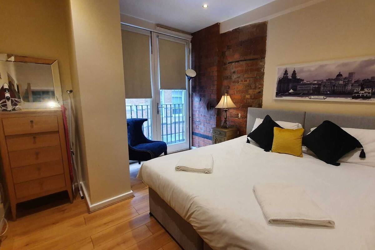 A hotel room with a bed, a dresser, a lamp, and a cityscape painting.