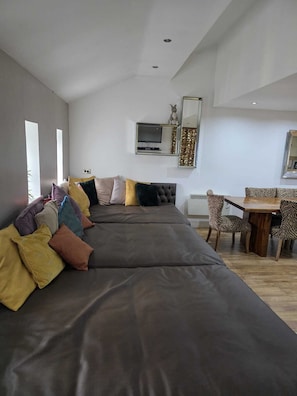 A modern living room with a long grey sofa, a dining table with zebra-patterned chairs, and a large mirror on the wall. - Contractor Mid week bookers (Liverpool)
