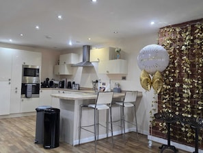 A modern kitchen with white cabinetry, a stainless steel range hood, and a central island with bar stools. - Contractor Mid week bookers (Liverpool)