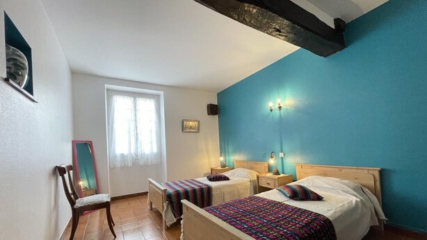 Un dormitorio con dos camas, una silla, un ventanal con cortinas y una pared de acento azul.