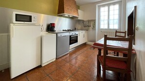 Cocina compacta con microondas, cafetera y estufa. Hay una mesa de comedor con sillas y un ventanal que proporciona luz natural.
