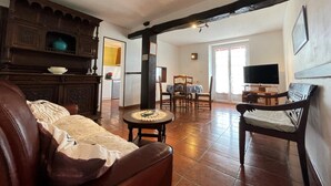 Sala de estar con sofá, mesa de centro y televisor. Se observa una cocina al fondo con mesa y sillas de comedor.