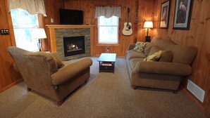 A cozy living room with a fireplace, wooden walls, a sofa, a chair, and a guitar.