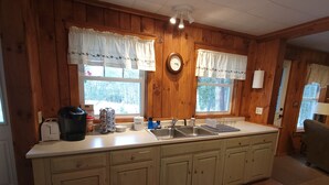A wooden-paneled kitchen with a large island, two windows with curtains, a clock, and basic kitchen appliances.