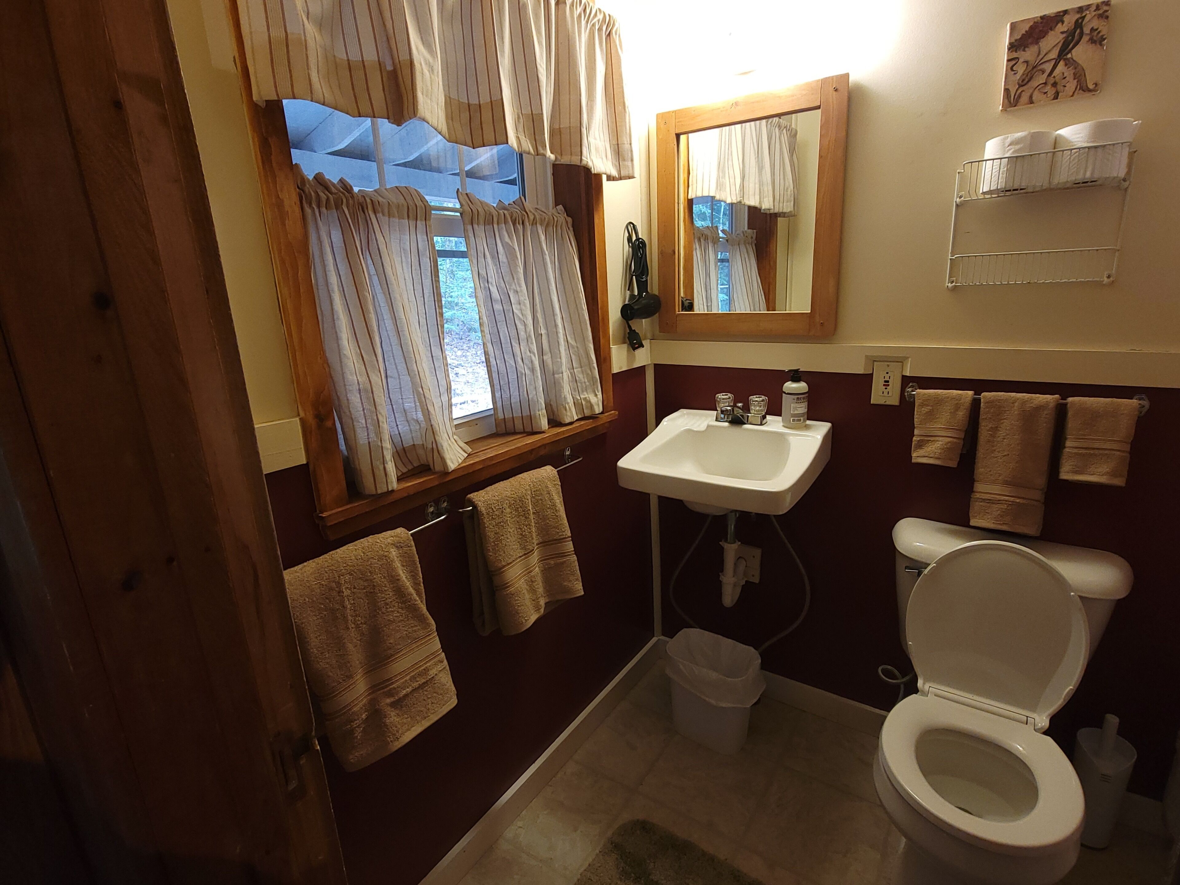 A bathroom with a sink, toilet, and window with curtains. There are towels hanging on the wall and a mirror above the sink.