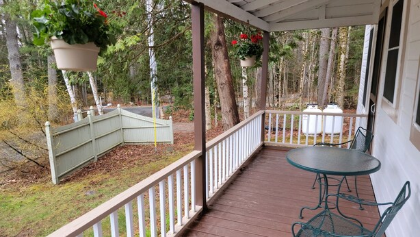 A covered porch with a table and chairs, surrounded by a white railing, and hanging flower pots.