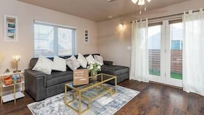 A living room with a grey sofa, a glass coffee table, a ceiling fan, and a view through a sliding glass door.