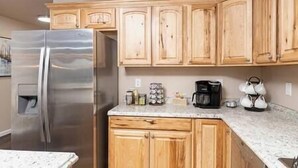 A kitchen with wooden cabinets, a stainless steel refrigerator, a coffee maker, and a kettle on the countertop.