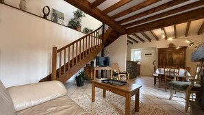 A spacious living area with a wooden staircase, a sofa, a coffee table, and a dining table with chairs.