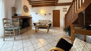 A living room with a fireplace, wooden beams, a sofa, a coffee table, and a staircase.